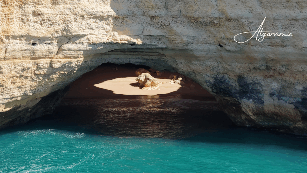 a cliff at and a cave entrance with ocean in front and the sun shining from the top into the cave